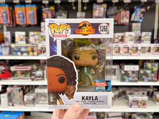 A Funko Pop toy held out by hand in front of a store shelf with other Funko Pop toys sitting on the store shelves.