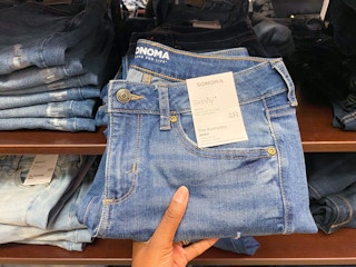 Hand holding a pair of Sonoma skinny jeans in front of a shelf with other jeans