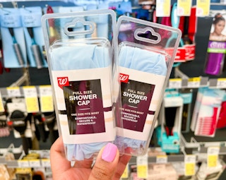hand holding two packs of Walgreens shower caps