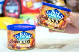 a hand holding on can of almonds next to another on a table