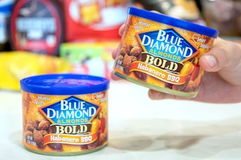 a hand holding on can of almonds next to another on a table
