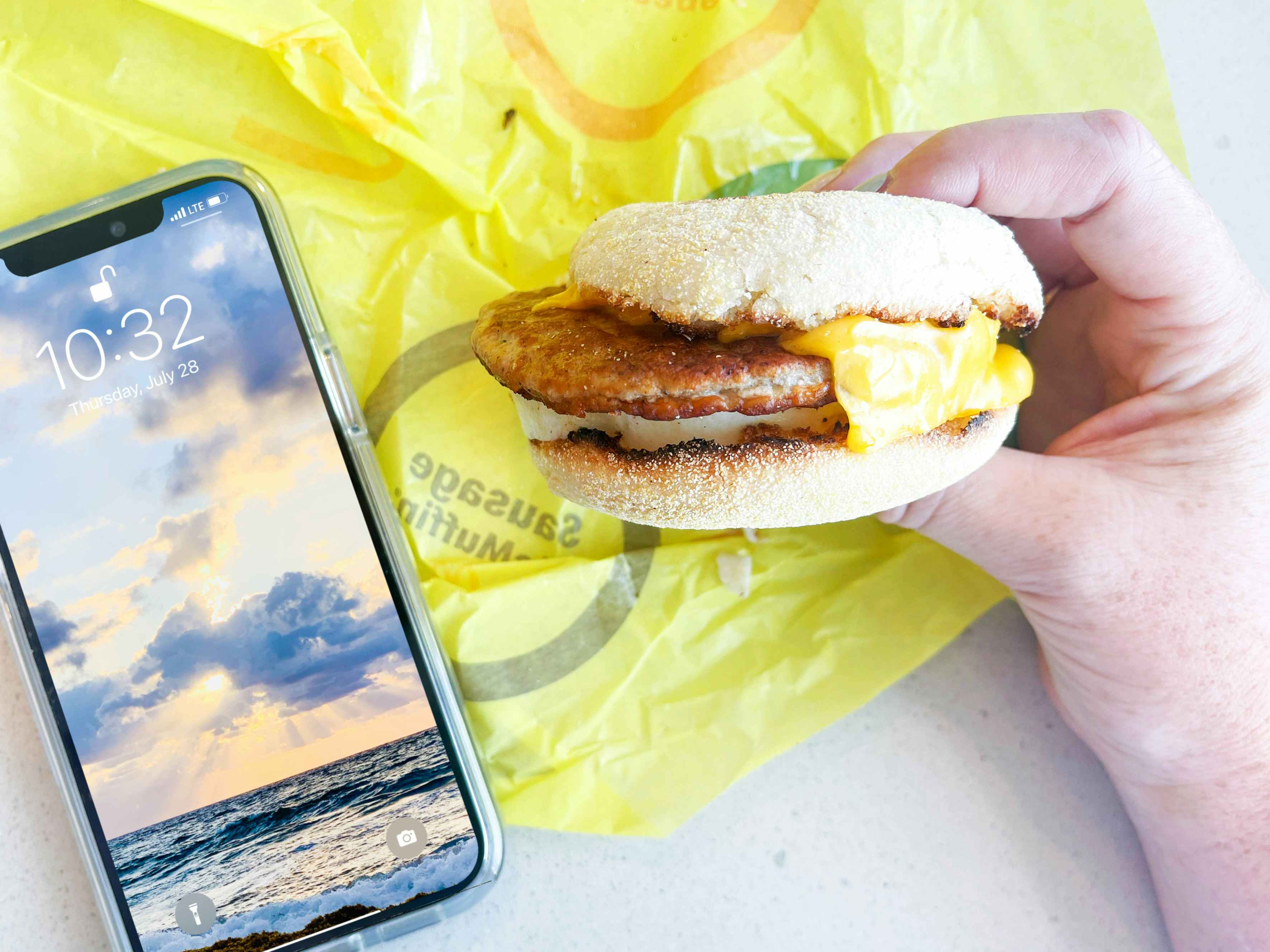 a mcmuffin being held with a cellphone on table with time
