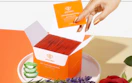 a hand pulling a pack of nail polish remover pads out of an orange box