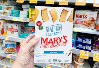 womans left hand holding a box of mary's gone crackers in front of other gluten free items on shelves at walmart