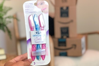 A hand holding Schick razors in front of Amazon boxes