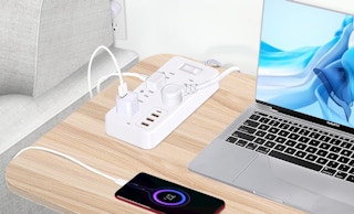 a power strip on a table with a laptop and a phone