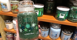 A hand holding a balsam and cedar scented Yankee Candle in a store.