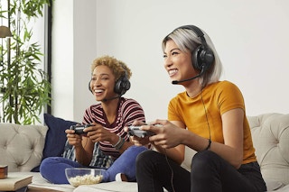 Two women playing video games with JBL gaming headphones on