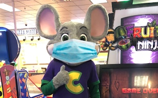 Chuck E. Cheese mouse character with a face mask for COVID-19 giving a thumbs up.