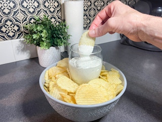 a hand dipping a chip into ranch dip from a wine glass filled with dip