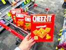 person holding a box of cheez-it crackers over a cart with more cheez-its in it