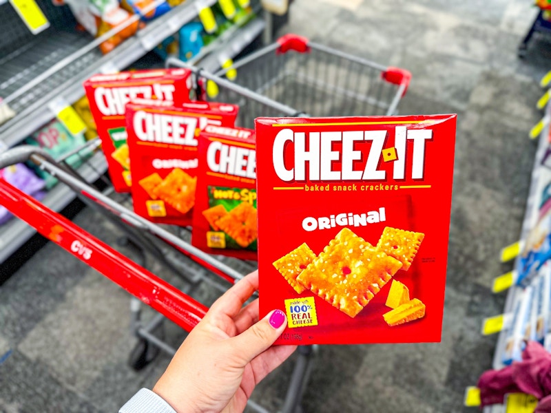 person holding a box of cheez-it crackers over a cart with more cheez-its in it
