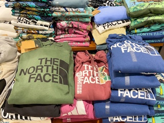 A variety of The North Face hoodies folded on a shelf at Dicks Sporting Goods