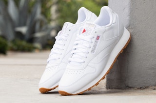 Two white leather Reebok Classic shoes (unisex) lean on a concrete block