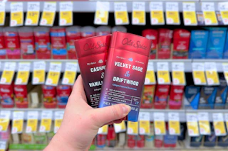 person holding 2 old spice alchemist deodorants in front of a shelf