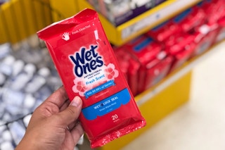 a hand holding a red pack of wet wipes