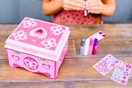 Lifestyle image of the Melissa & Doug Jewelry Craft kit being used by a child in the background