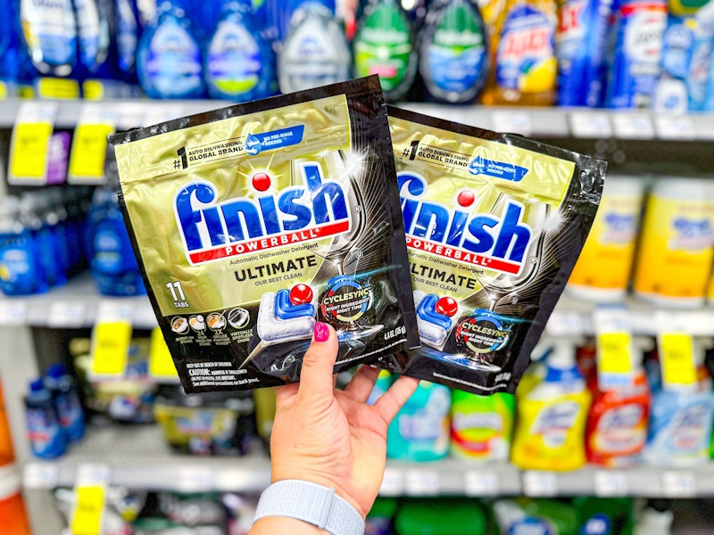 person holding 2 bags of finish dishwasher tabs in front of the shelf