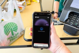 A person's hand holding a cellphone with apple pay on screen at the dollar tree register about to pay.