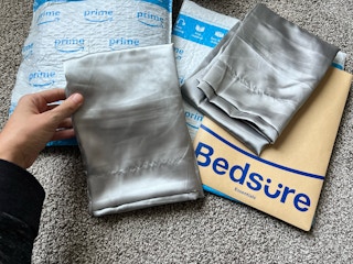 two grey satin pillowcases on top of packaging on the floor