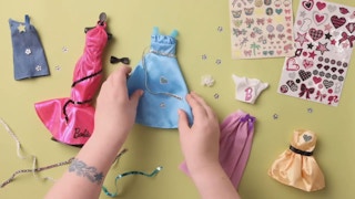 A child customizing Barbie dresses with stickers.