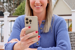 A woman in a periwinkle top smiles down at her phone