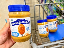 hand holding a jar of peanut butter and co spread over walmart cart