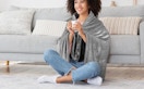 a person wearing a grey heated blanket sitting in front of a couch