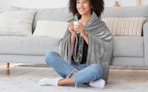 a person wearing a grey heated blanket sitting in front of a couch