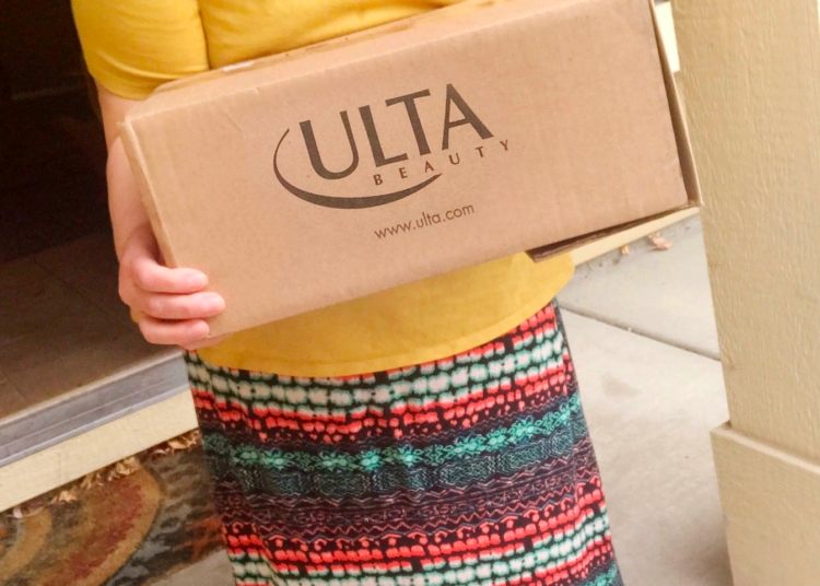 A person holding an Ulta delivery box on a doorstep.