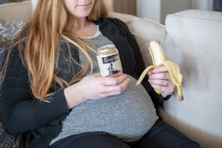 A pregnant woman holding a ginger beer in one hand and a banana in the other hand.