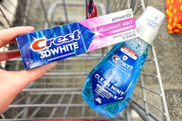person holding crest toothpaste over crest mouthwash in a cart