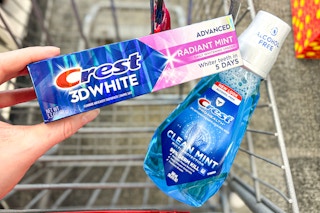person holding crest toothpaste over crest mouthwash in a cart
