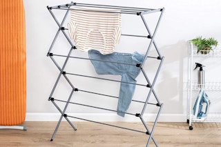 A Honey-Can-Do collapsible clothing drying rack in a room with clothes on it
