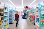 Two women inside Walgreens, one of them posing and the other one jumping into the air.