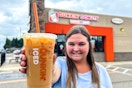 a person standing outside of dunkin with an iced coffee