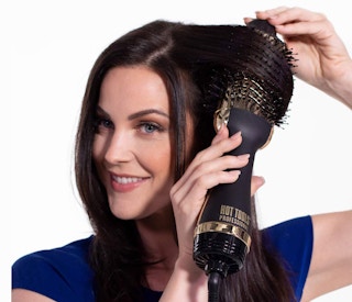 A woman using a golden Hot Tools hair dryer brush on her hair.