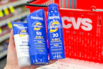 hand holding coppertone sunscreens in front of a cvs shopping basket