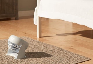 a fan on the floor next to a bed in a room