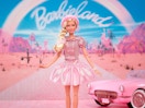 a barbie the movie doll in front of a pink car