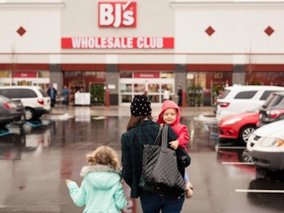 Woman and two children walking toward a BJ's Wholesale Club store across the parking lot.