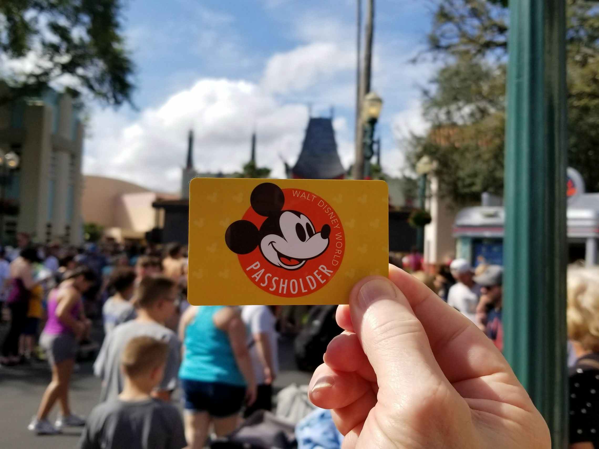 A Disney World annual passholder card held up with a Disney park in the background.
