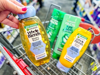 person holding a garnier whole blends shampoo in front of a cart with more garnier shampoo in it