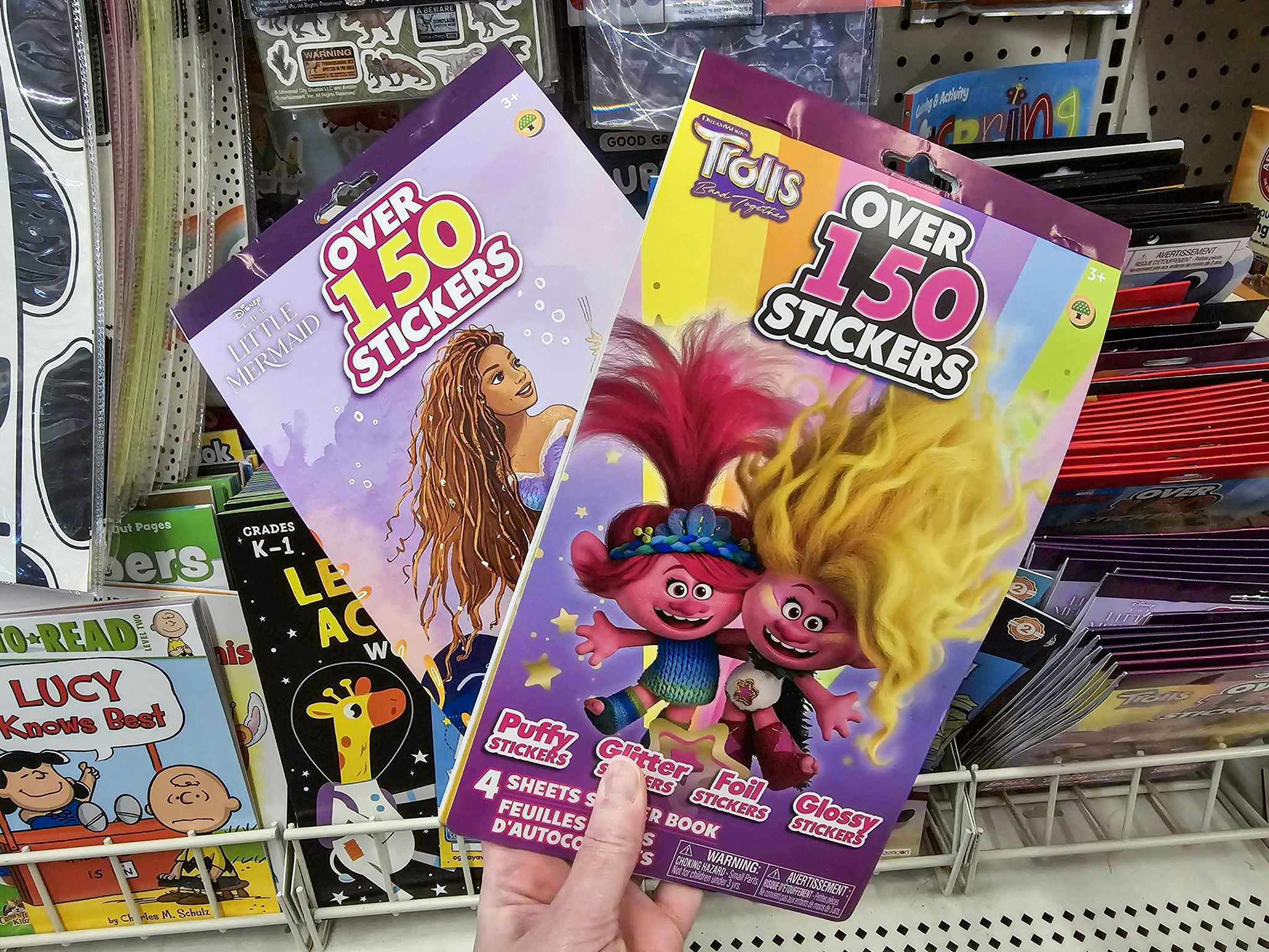 person holding  little mermaid and trolls sticker books