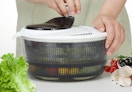 a person using a salad spinner with veggies inside