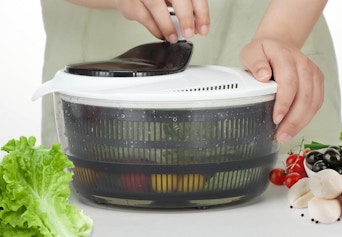 a person using a salad spinner with veggies inside