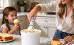 a mom scooping ice cream out off a bucket next to a little kid with an ice cream cone