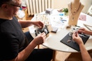 Two people sitting at a table and making jewelry.