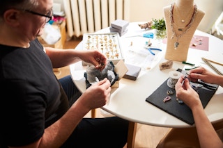 Two people sitting at a table and making jewelry.