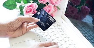 hand holding american express cash preferred card near laptop and flowers